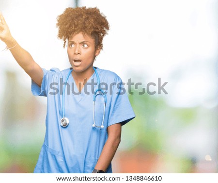 Young african american doctor woman over isolated background Pointing with finger surprised ahead, open mouth amazed expression, something in front