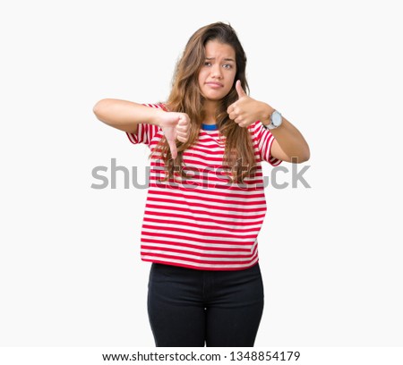 Young beautiful brunette woman wearing stripes t-shirt over isolated background Doing thumbs up and down, disagreement and agreement expression. Crazy conflict