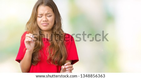 Young beautiful brunette woman wearing red t-shirt over isolated background disgusted expression, displeased and fearful doing disgust face because aversion reaction. With hands raised. Annoying