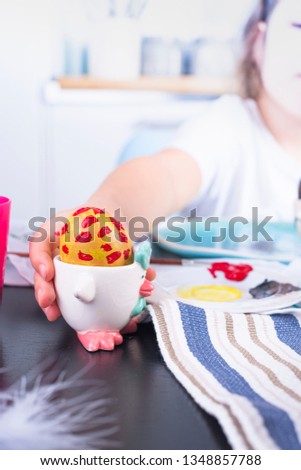 Little girl paints eggs for Easter in the kitchen at home. Child and holiday items of spring. A happy child draws. Copy space