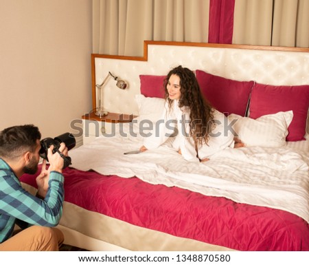 Young beautiful model posing in a bed for professional photographer in hotel room