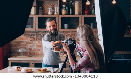 Woman shooting food blogger. Photo session. Man at kitchen counter with plate of fresh pastries. Have a treat. Backstage photography.