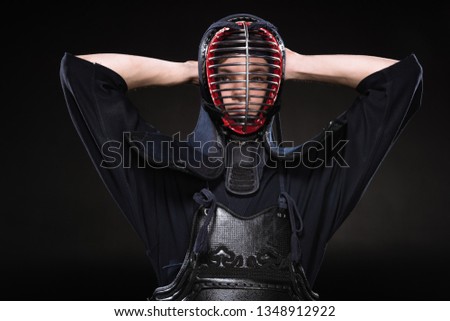 Kendo fighter in armor touching helmet and looking at camera on black
