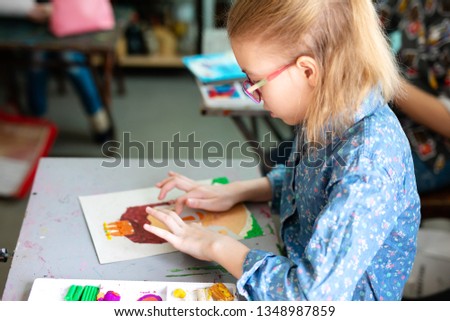 Portrait of adorable little girl smiling happily while enjoying art and craft lesson in art school working together with other kids. Pictures from modeling clay