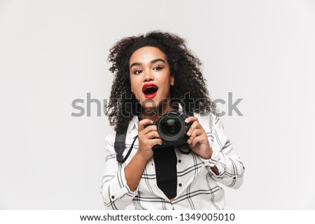 Portrait of a cheerful afro american woman standing isolated over white background, using photo camera