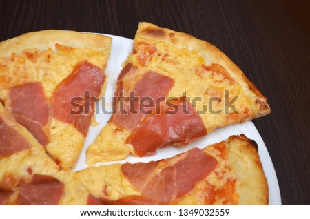 Pizza with cheese and prosciutto in a white plate on a dark wooden table, one piece cut off