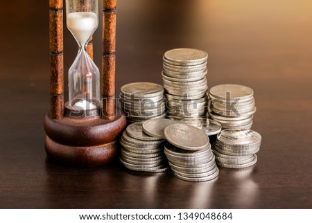 Stack of coins with hourglass on wood table