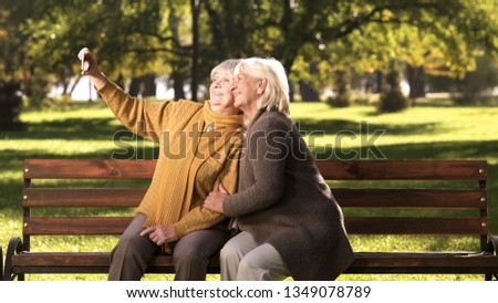 Two old ladies taking selfie on mobile phone sitting on bench in park technology