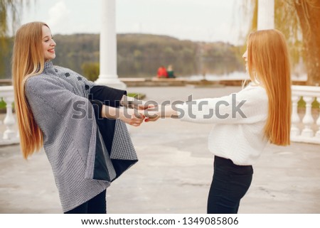 a cute and beautiful girl with long, bright hair, dressed in a gray coat, walks along with her younger sister, who also has long, bright hair, they walk in the autumn park