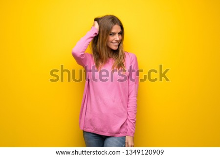 Woman with pink sweater over yellow wall thinking an idea while scratching head