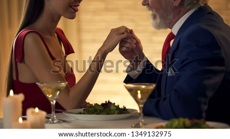 Senior gentleman holding hand of tender young wife, romantic date together Royalty-Free Stock Photo #1349132975