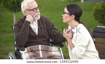 Worried young woman comforting sick grandfather sitting in wheelchair, hospital