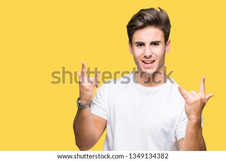 Young handsome man wearing white t-shirt over isolated background shouting with crazy expression doing rock symbol with hands up. Music star. Heavy concept.