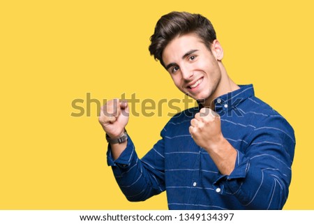 Young handsome man wearing navy shirt over isolated background very happy and excited doing winner gesture with arms raised, smiling and screaming for success. Celebration concept.
