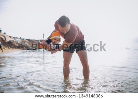 Young father playing with his small boy child near the sea at sunset