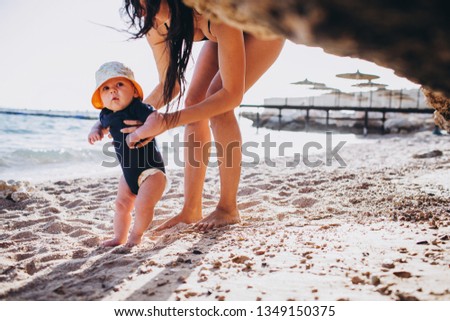 Young mother at swimwear playing with her son at the sea, teaching him to walk