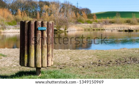 Wooden Litter bin located on green grass with a lake and trees in the background.  Shot taken on a sunny warm day at Herrington Country Park, Sunderland.