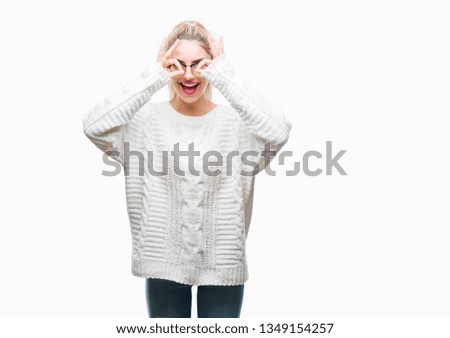 Young beautiful blonde woman wearing glasses over isolated background doing ok gesture like binoculars sticking tongue out, eyes looking through fingers. Crazy expression.