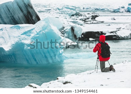 Photographer in red coat taking pictures of glacier ice