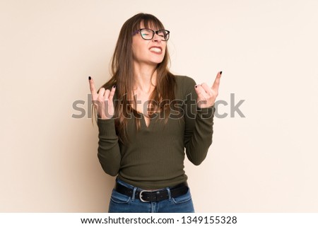 Young woman on ocher background making rock gesture
