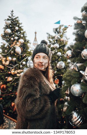 German good-looking young girl enjoying her time in Moscow through winter holiday  on New Year's Fair, drinking coffee and eating lollipop in front of Christmas Fair 