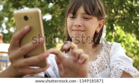 happy girl using smartphone scrolls through pages in the online store in the park on the bench. Young millennial woman in the Arboretum, making gestures on phone display.