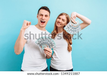 Photo of a happy young couple in love, man and woman, dressed in white T-shirts, holding money in their hands, on a blue background