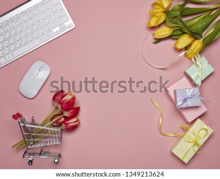 Shopping trolley, gift boxes, tulips flowers, computer keyboard and mouse on pink background. Top view with copy space. Valentine's day, Mother's day, Women's day, wedding. Seasonal sale