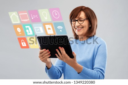 technology, automation and internet of things concept - smiling senior woman in glasses with tablet computer using smart home app over grey background