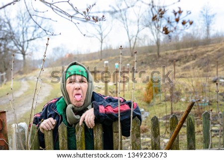 The poor rural grandmother shows the tongue near her fence, showing malice to everyone else