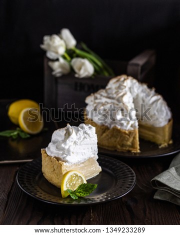 Lemon cake with snow-white meringue on a wooden table with tulips in the background. Dark food photo.