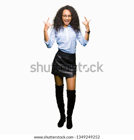 Young beautiful business girl with curly hair wearing glasses shouting with crazy expression doing rock symbol with hands up. Music star. Heavy concept.