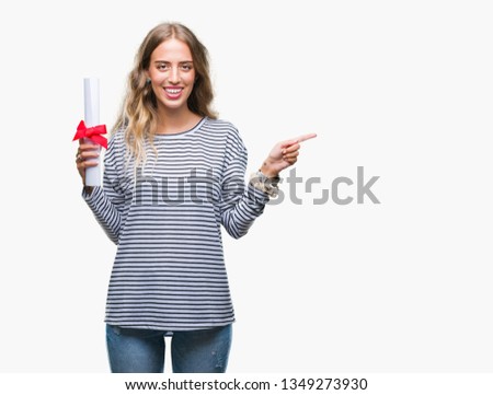 Beautiful young blonde woman holding degree certificate over isolated background very happy pointing with hand and finger to the side