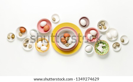 Easter home decor concept, view from above on various types of plates and bowls filled with natural eggs, blank space for a text
