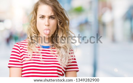 Beautiful young blonde woman over isolated background sticking tongue out happy with funny expression. Emotion concept.