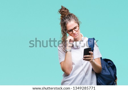 Young brunette student girl wearing backpack, headphones and smartphone over isolated background serious face thinking about question, very confused idea