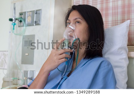 Sick beautiful female in blue cloth hold nasal mask with respiratory problem in hospital room. Asian woman patient inhalation therapy by the mask of inhaler with soft stream smoke from bronchodilator. Royalty-Free Stock Photo #1349289188