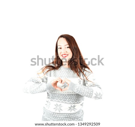 Happy young woman smiling and doing a heart shape with both her hands while wearing a grey jumper against a white background