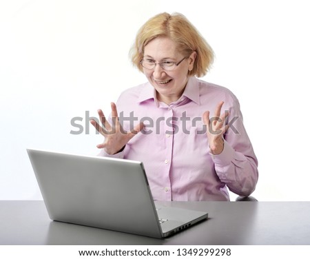 A blonde woman in glasses and a pink shirt sits at the table, with delight looking at monitor laptop