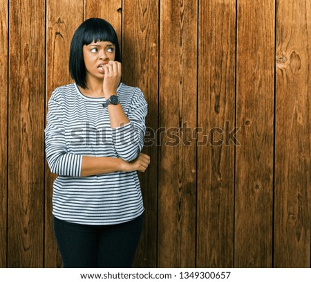 Beautiful young african american woman wearing stripes sweater over isolated background looking stressed and nervous with hands on mouth biting nails. Anxiety problem.