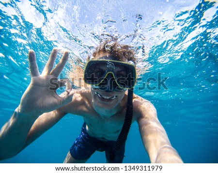 boy with mask and flippers swim in clear blue water and taking a self portrait picture