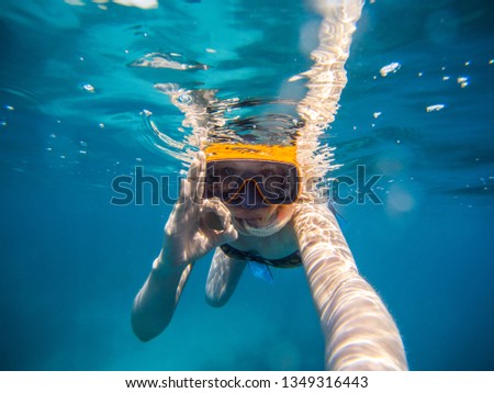 Girl with mask and flippers swim in clear blue water and taking a self portrait picture
