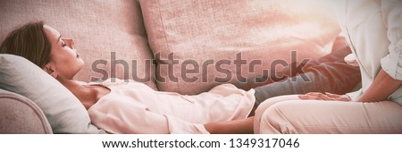 Hypnotherapist holding pendulum by patient on sofa at home Royalty-Free Stock Photo #1349317046