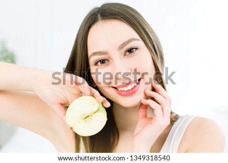 Beautiful smile, white strong teeth. Head and shoulders of young woman with snow-white smile holding green apple, teethcare.