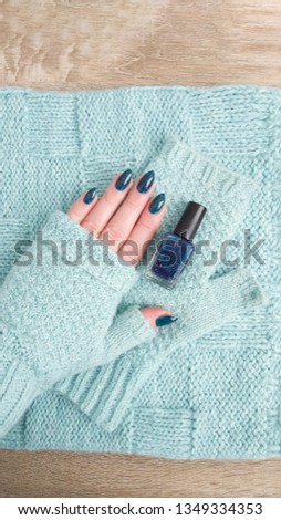 Female hand with turquoise teal long nails and a bottle of nail polish