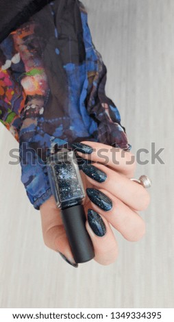 Female hand with turquoise teal long nails and a bottle of nail polish