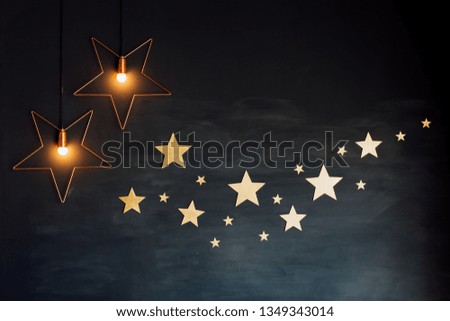 Multiple golden metal stars and lit bulbs hanging on a black grunge wall as decoration. Starry night loft design.