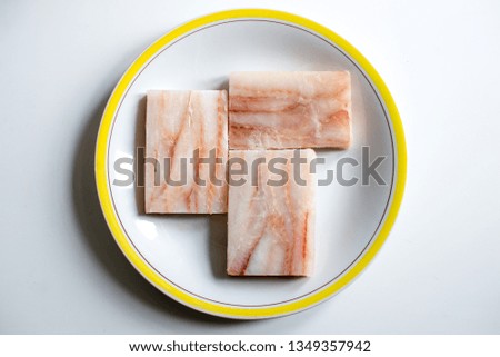 Raw fillets of cod cubes isolated on a plate on white background. 