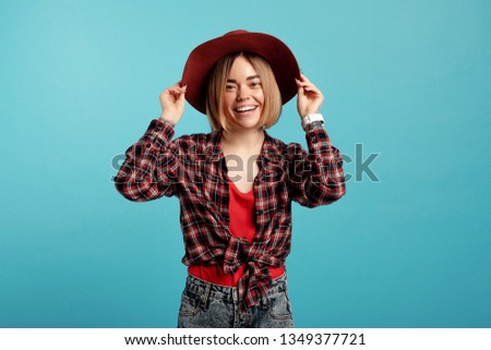Nice young woman pose on camera and smile. She hold hat. Isolated over blue background