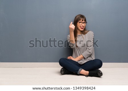 Woman with glasses sitting on the floor making money gesture